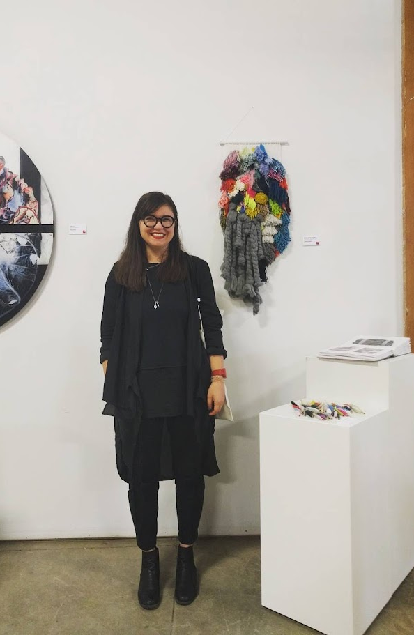 Varvara Zhemchuzhnikova in the gallery beside one of her Social Ryijy tapestries