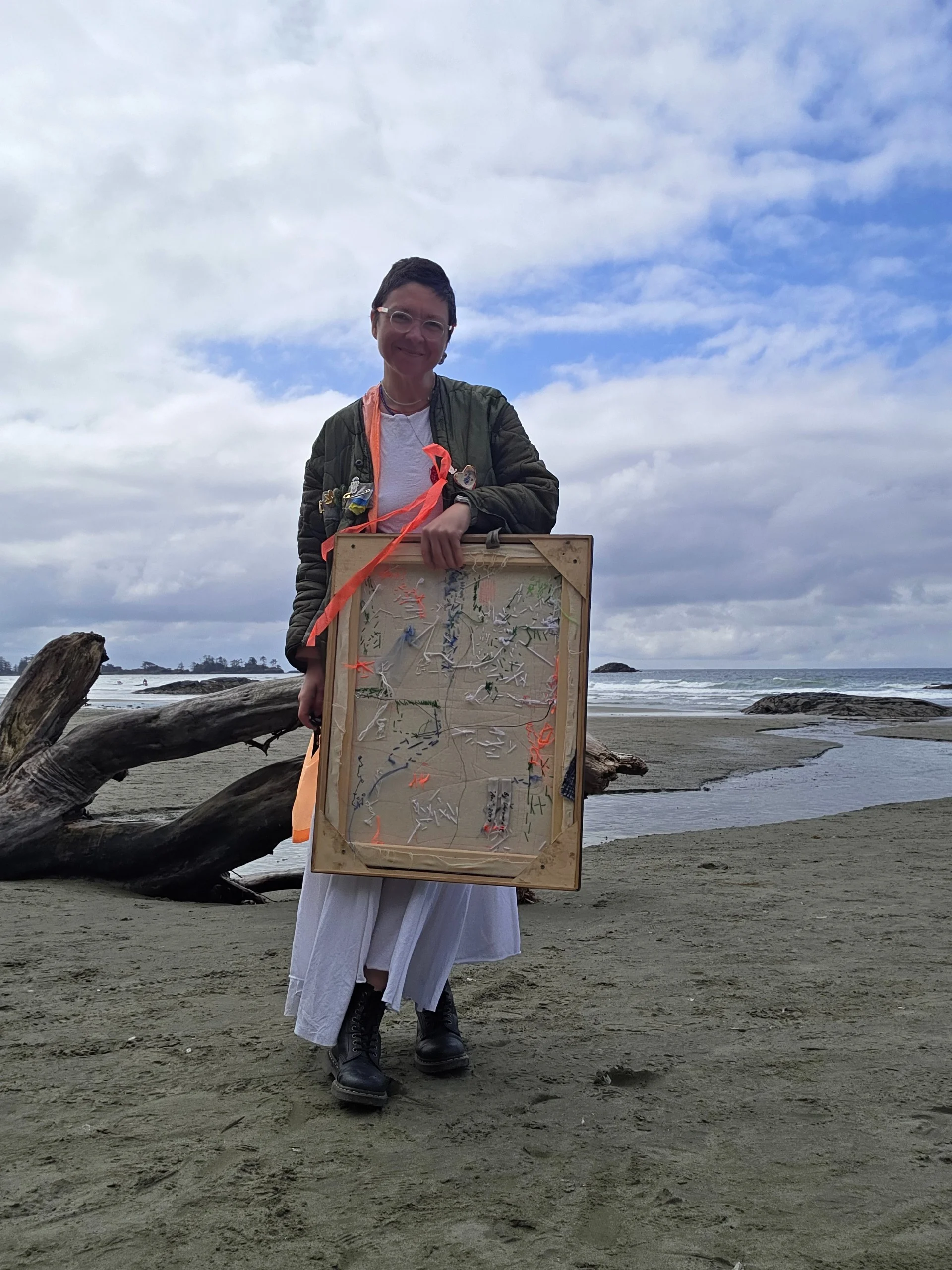 Varvara on the beach holding the artwork, its stitched reverse visible