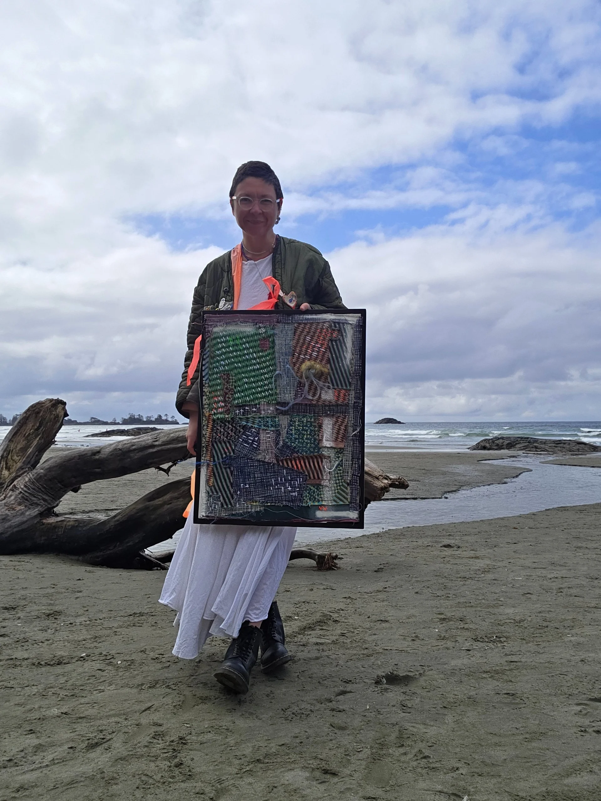 Varvara standing on a beach holding the framed artwork facing the camera