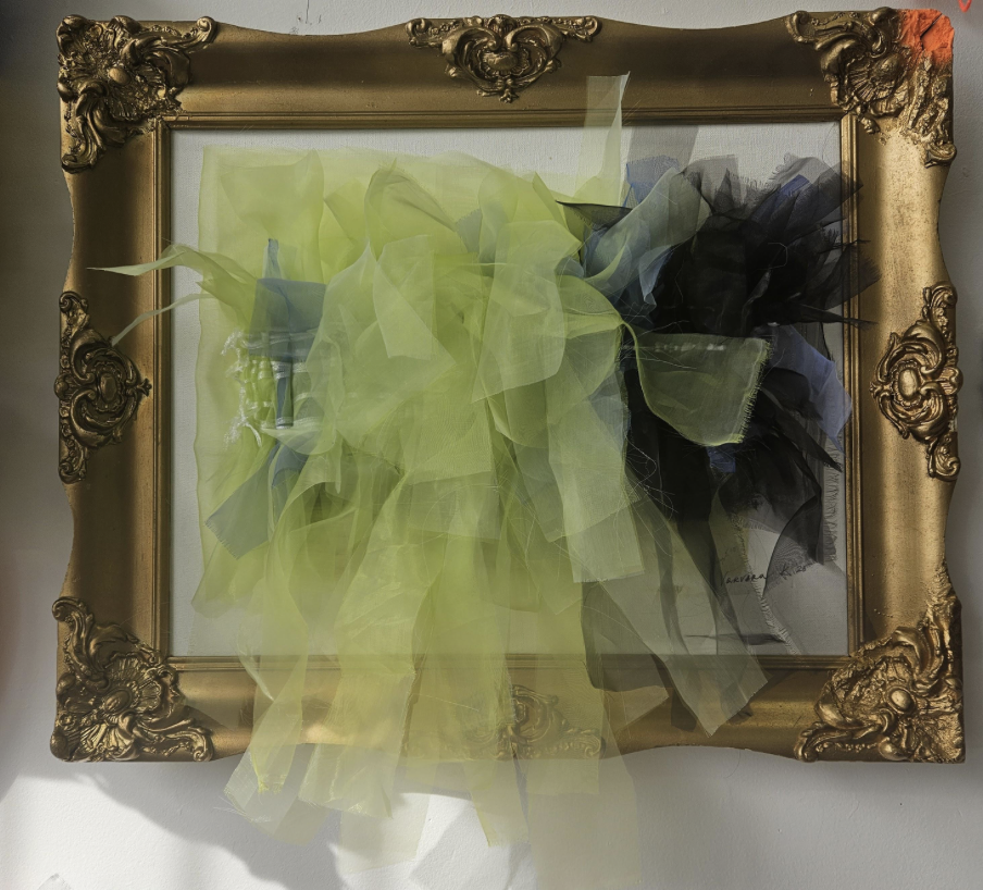 The framed piece in daylight, the green and dark tulle weave glowing translucent against the white canvas